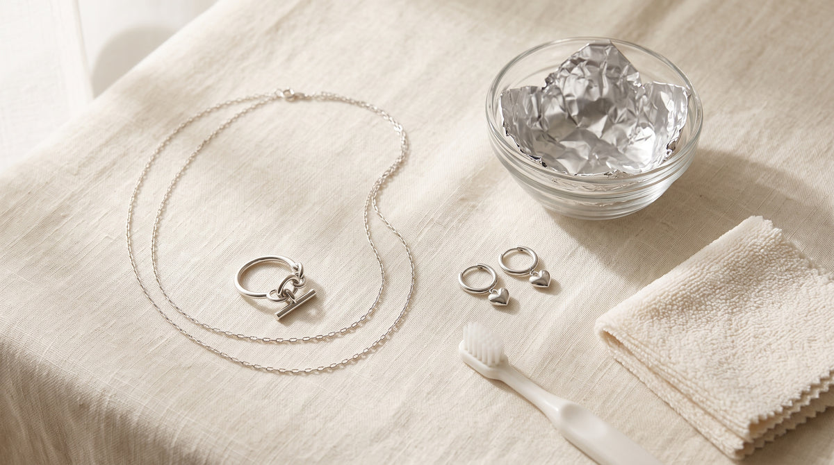 Silver chain, chain ring and heart earrings beside a foil-lined bowl and soft cloth: how to clean silver jewelry
