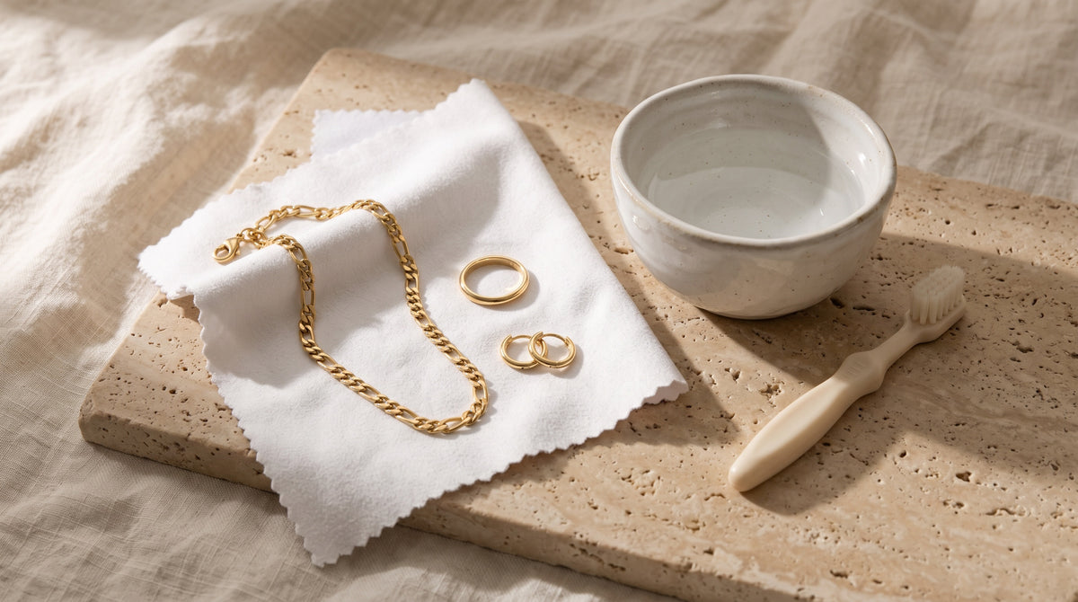 Gold figaro chain, band ring and huggie hoops on a microfiber cloth by a bowl: how to clean gold jewelry