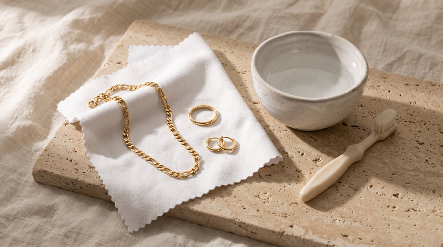 Gold figaro chain, band ring and huggie hoops on a microfiber cloth by a bowl: how to clean gold jewelry