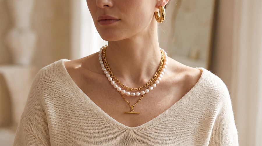 Woman wearing chunky gold hoops, a layered gold necklace and baroque pearls, three key jewelry trends