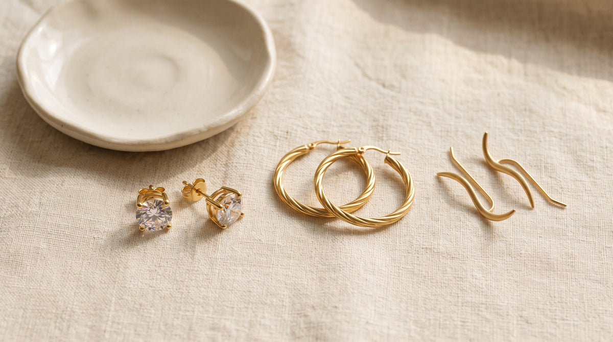 Types of earrings side by side: stud earrings, twisted hoops and wave ear climbers on cream linen