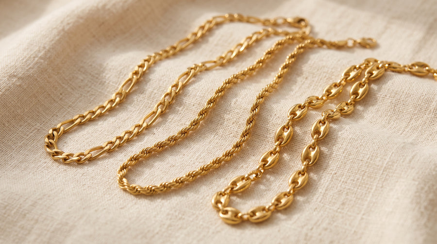 Three types of chains, figaro, rope and coffee bean, laid side by side on cream linen