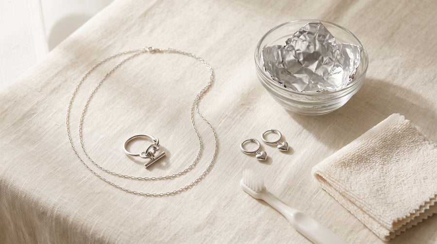 Silver chain, chain ring and heart earrings beside a foil-lined bowl and soft cloth: how to clean silver jewelry