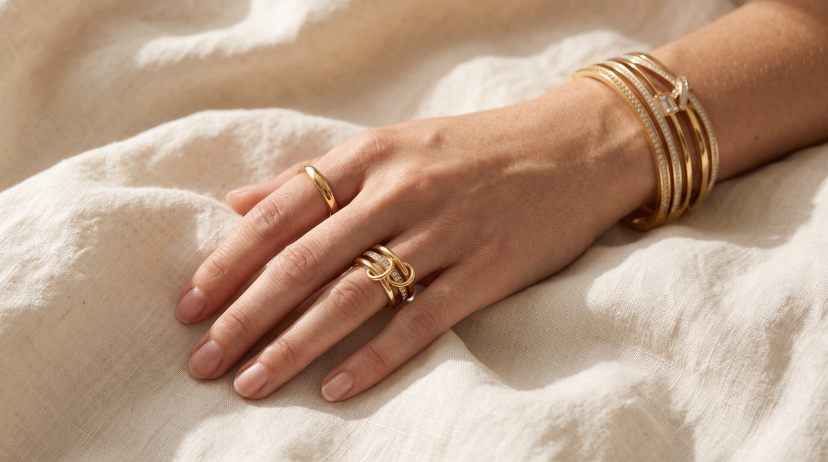 Hand with gold band and interlocking rings plus stacked gold bangles, showing how to stack rings