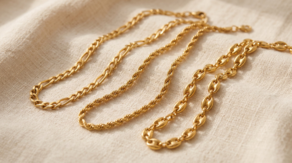 Three types of chains, figaro, rope and coffee bean, laid side by side on cream linen