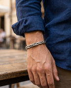 Twisted silver bangle worn on a man's wrist with a gray T-shirt