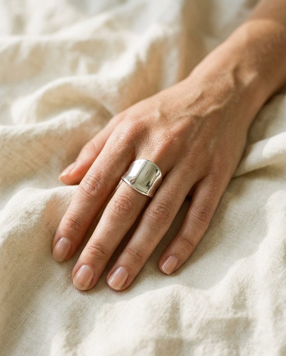 Wide silver ring worn on the thumb with fine rings on other fingers