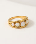 Opal ring with a row of white opals on a wide gold band, packshot