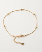 Gold anklet with small round beads on a white background