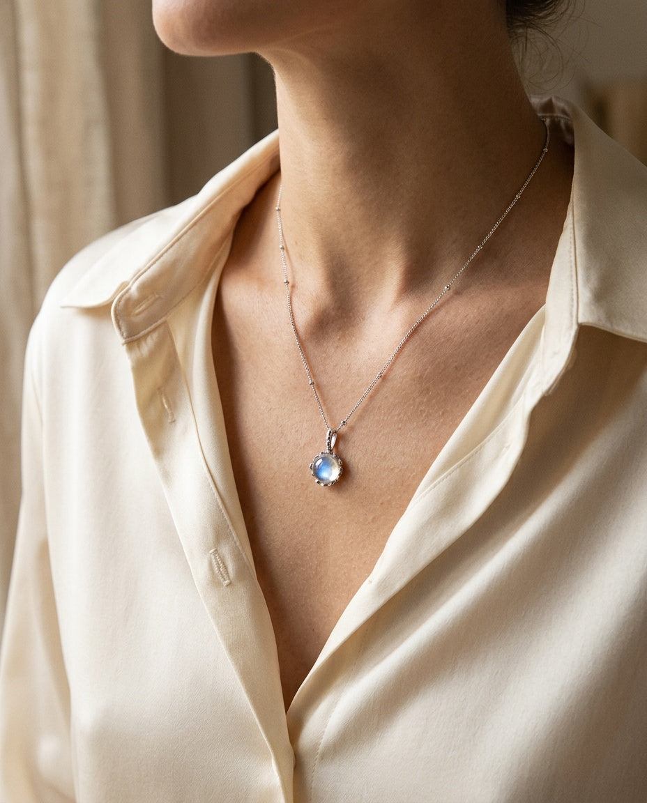 Pendentif rond bleuté porté sur les clavicules avec un caraco blanc