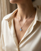 Pendentif rond bleuté porté sur les clavicules avec un caraco blanc