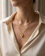 Heart necklace worn with an open collar, two layers visible