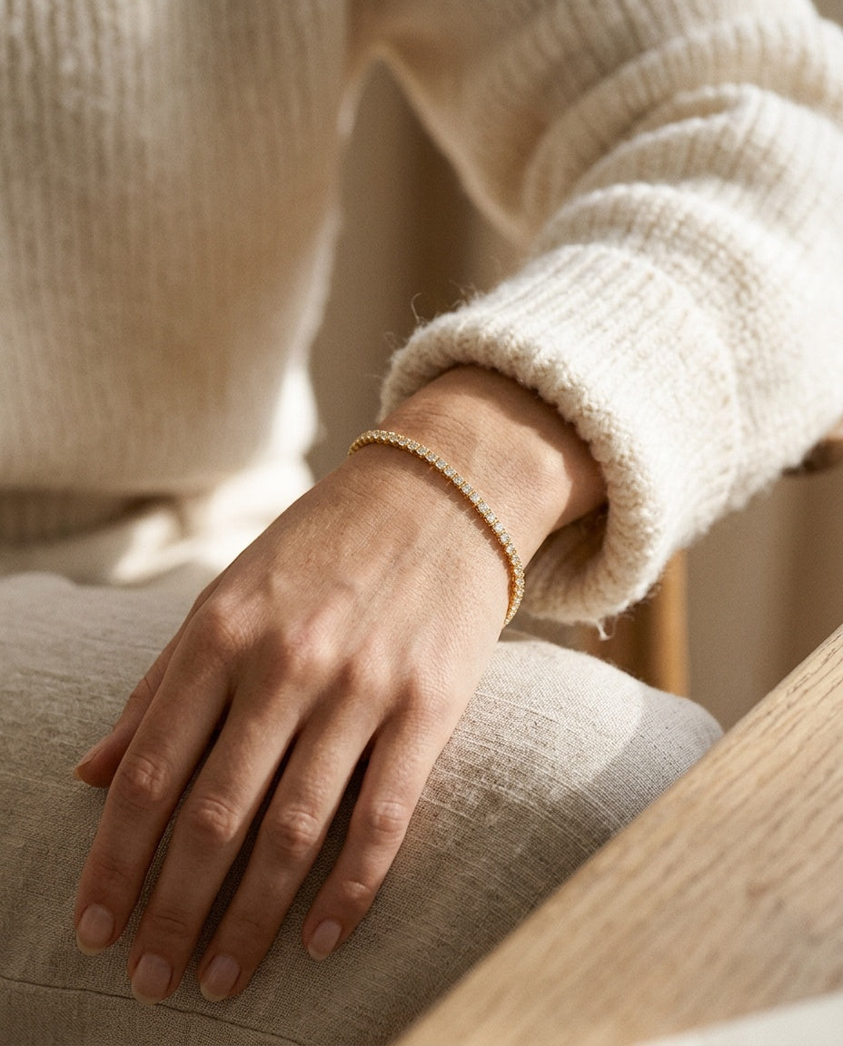 Gold tennis bracelet worn on the wrist next to a watch