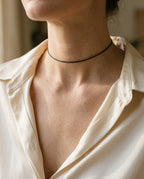 Woman in a white shirt wearing a thin black cord at the base of her neck