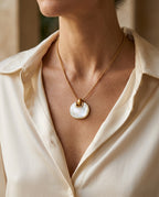 Round shell pendant worn at the base of the neck