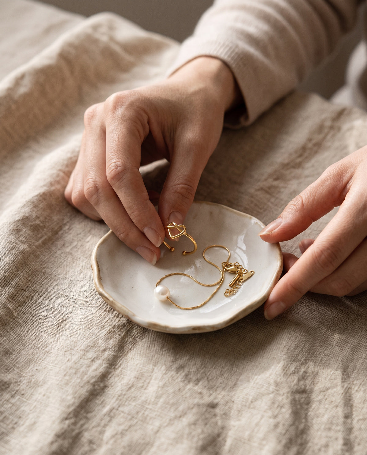 Hands placing gold jewelry in a porcelain dish